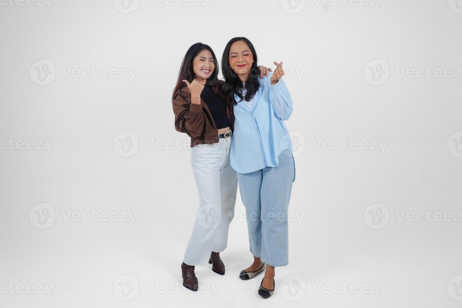 Two young Asian women expressing their tender feelings, shapes heart gesture expresses her love, isolated by white background. Friendship concept. photo