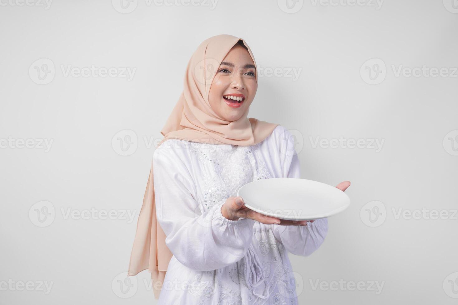 hermosa joven asiático musulmán mujer en hijab presentación un vacío plato con Copiar espacio terminado él, demostración el comida menú para iftar foto