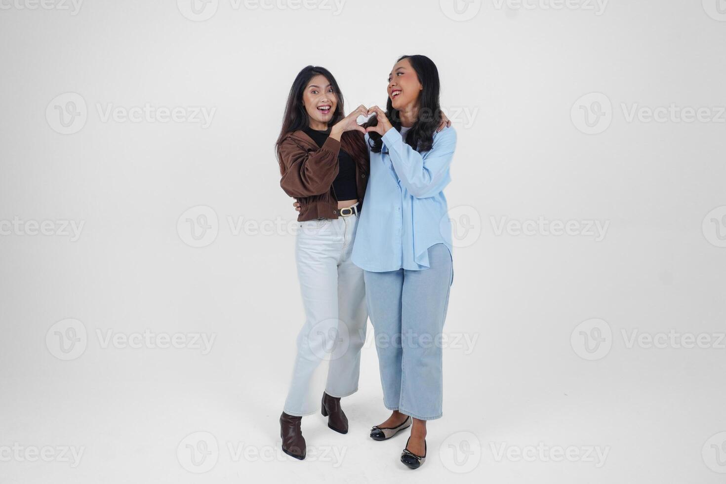 Two young Asian women expressing their tender feelings, shapes heart gesture expresses her love, isolated by white background. Friendship concept. photo