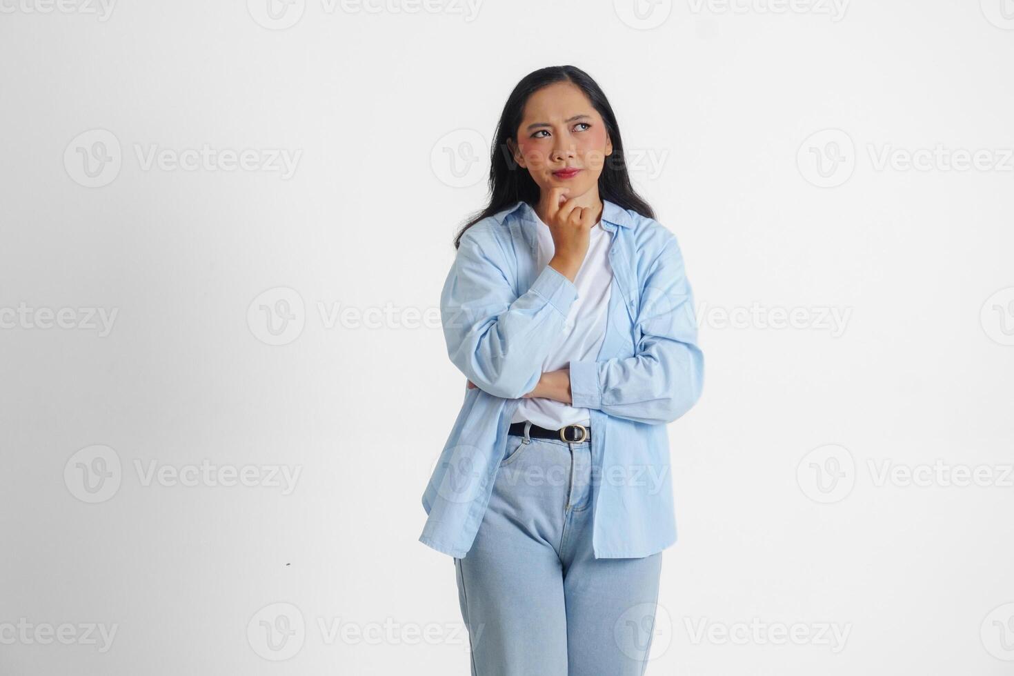 A thoughtful Asian woman wearing blue shirt is imagining her thoughts, isolated by white background. photo