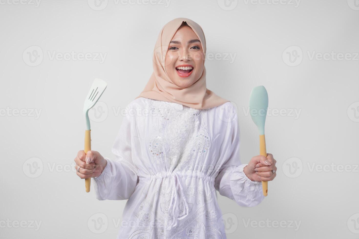 retrato de un contento asiático musulmán mujer en velo hijab participación espátula y cocina Cocinando utensilios mientras sonriente alegremente Ramadán concepto foto