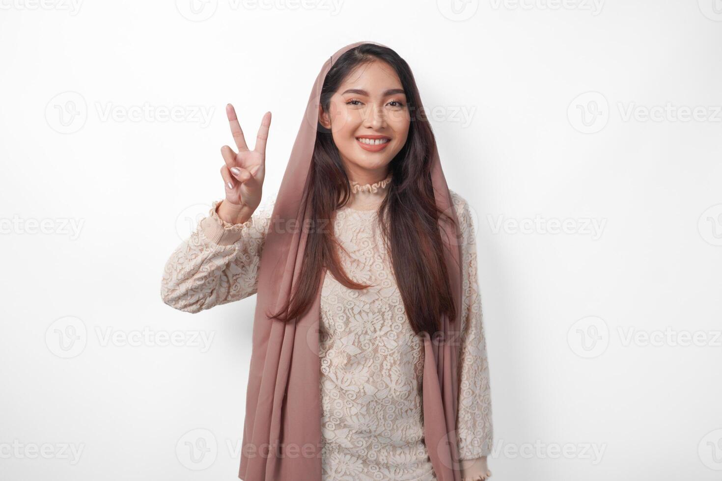 Portrait of attractive Asian Muslim woman wearing veil hijab giving number one to ten by hand gesture, standing over isolated white background photo