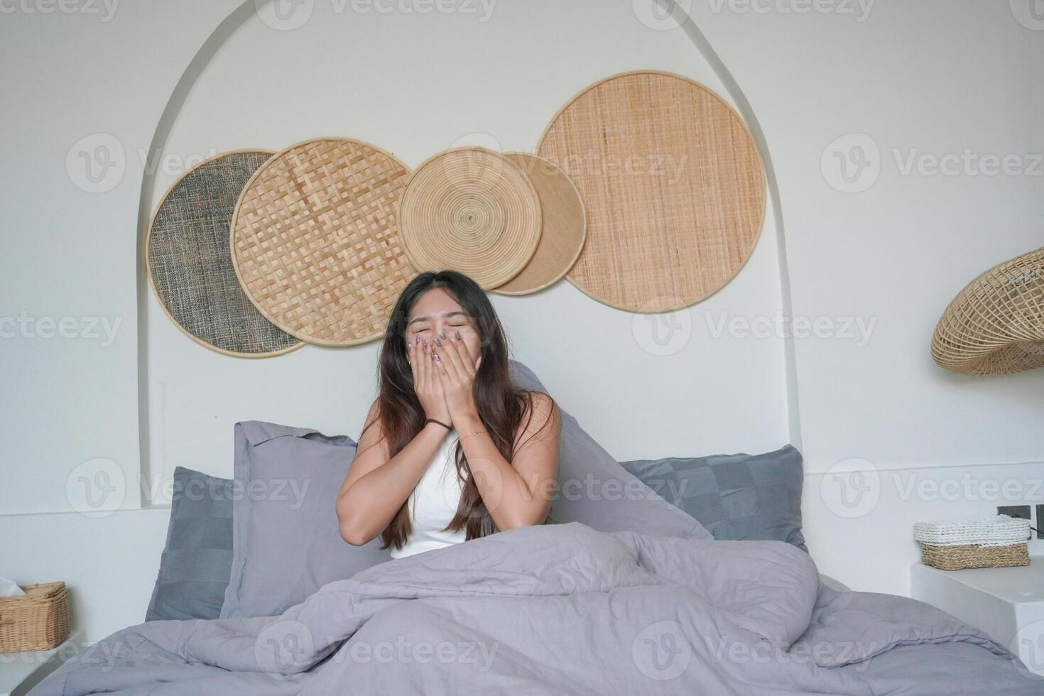 Sleepy Asian young woman yawning and raising hand waking up in early morning after deep sleep, peaceful morning holiday concept photo