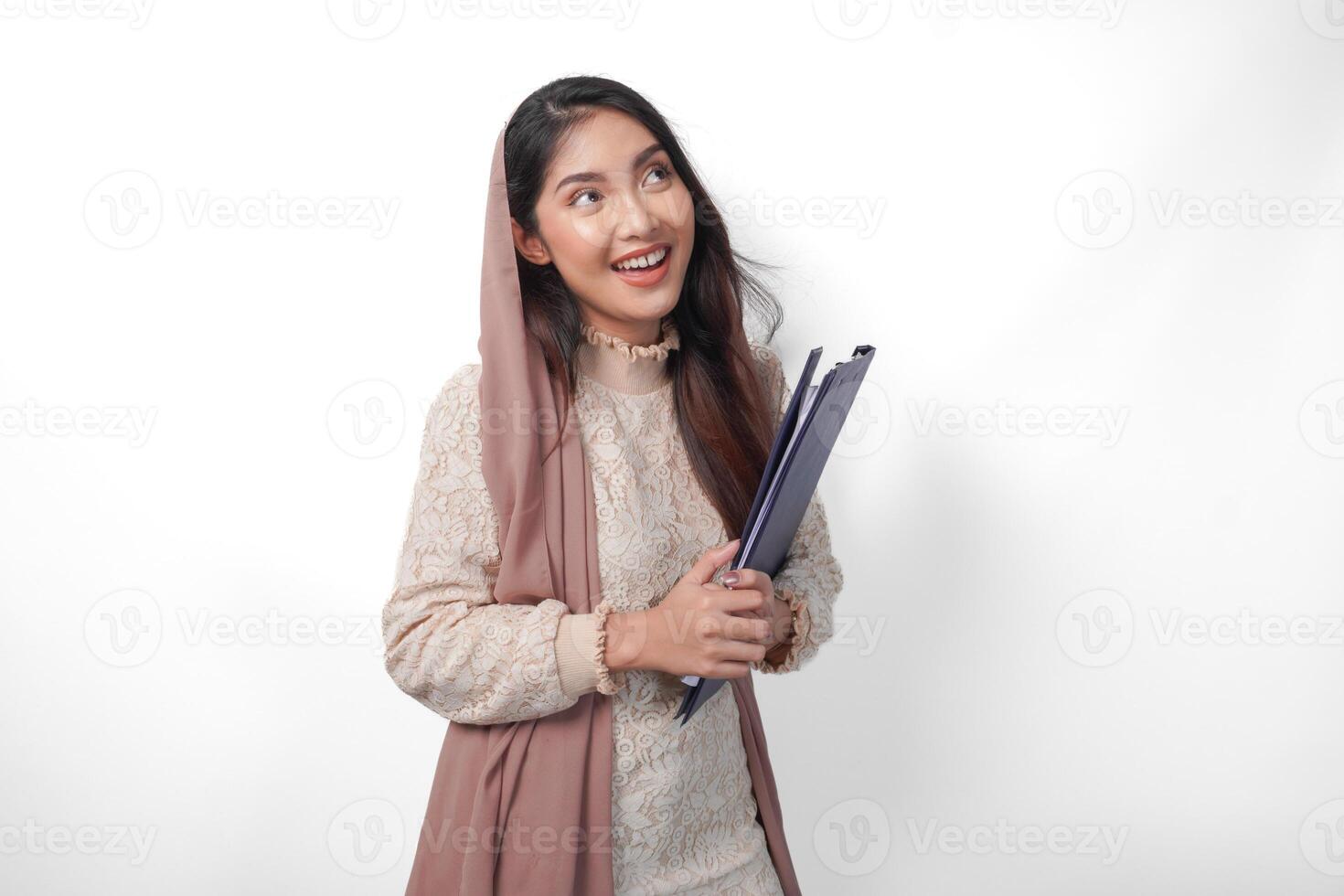 retrato de asiático musulmán mujer en Pañuelo velo hijab en pie y sonriente felizmente mientras participación un documento mapa. Ramadán concepto foto