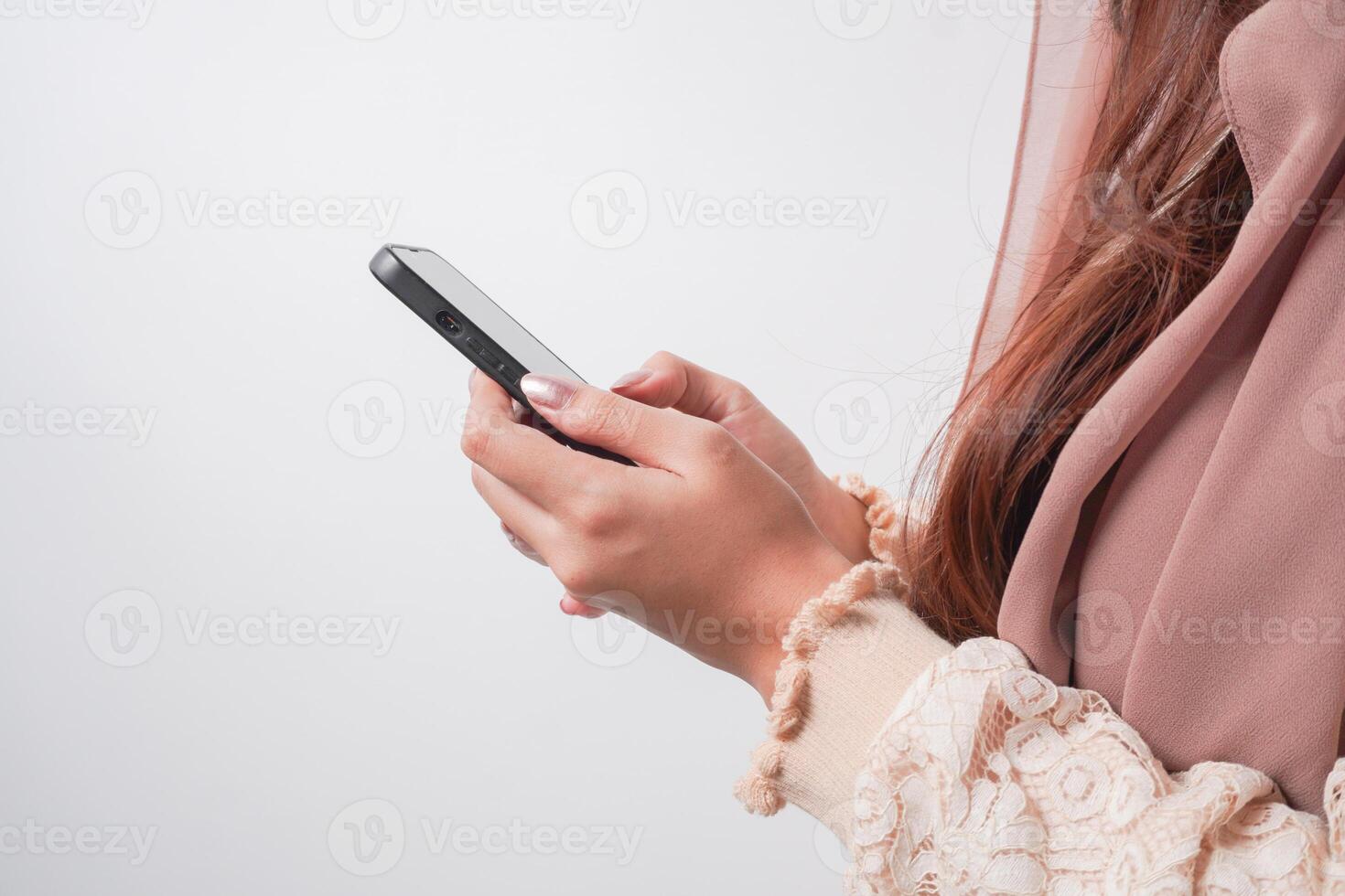 Close up portrait of Asian Muslim woman in headscarf veil hijab holding and using smartphone over isolated white background. Ramadan and Eid Mubarak concept. photo