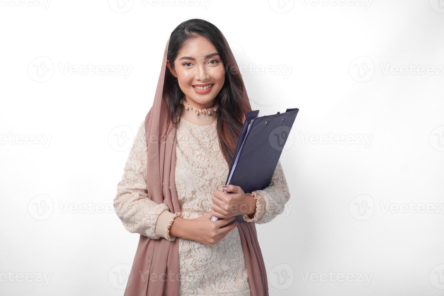 retrato de asiático musulmán mujer en Pañuelo velo hijab en pie y sonriente felizmente mientras participación un documento mapa. Ramadán concepto foto