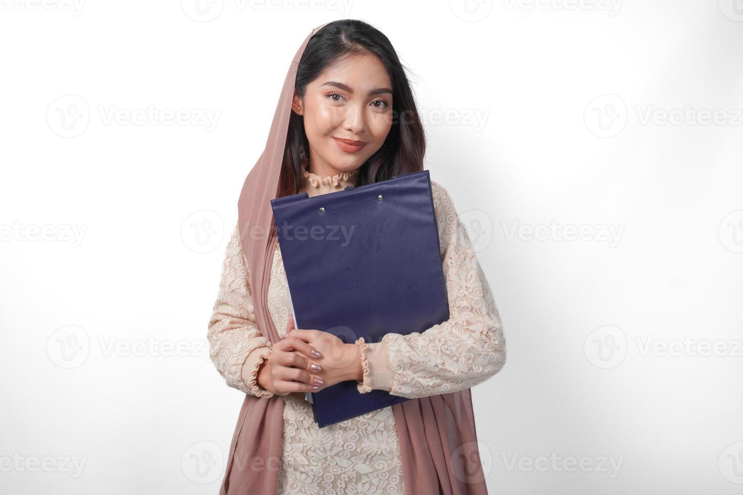 retrato de asiático musulmán mujer en Pañuelo velo hijab en pie y sonriente felizmente mientras participación un documento mapa. Ramadán concepto foto
