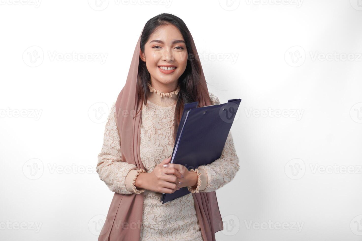 retrato de asiático musulmán mujer en Pañuelo velo hijab en pie y sonriente felizmente mientras participación un documento mapa. Ramadán concepto foto