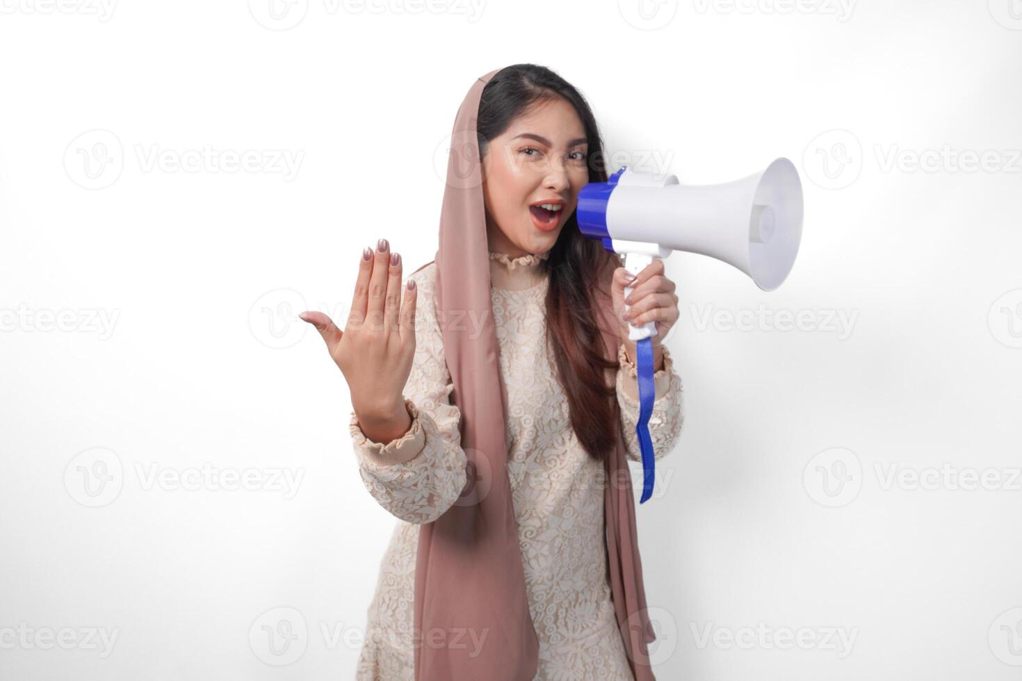 Energetic Asian Muslim woman wearing veil hijab shouting at megaphone while raising hand as inviting or lets go gesture. Ramadan and Eid Mubarak concept photo