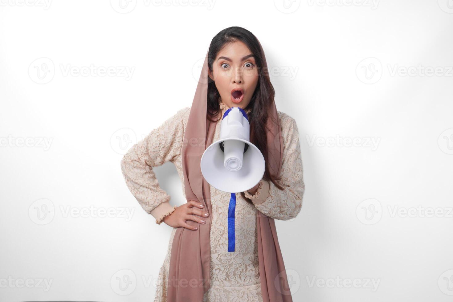 Lively Young Asian muslim woman wearing headscarf veil hijab shouting at megaphone, isolated on white background studio. Ramadan and Eid Mubarak concept. photo