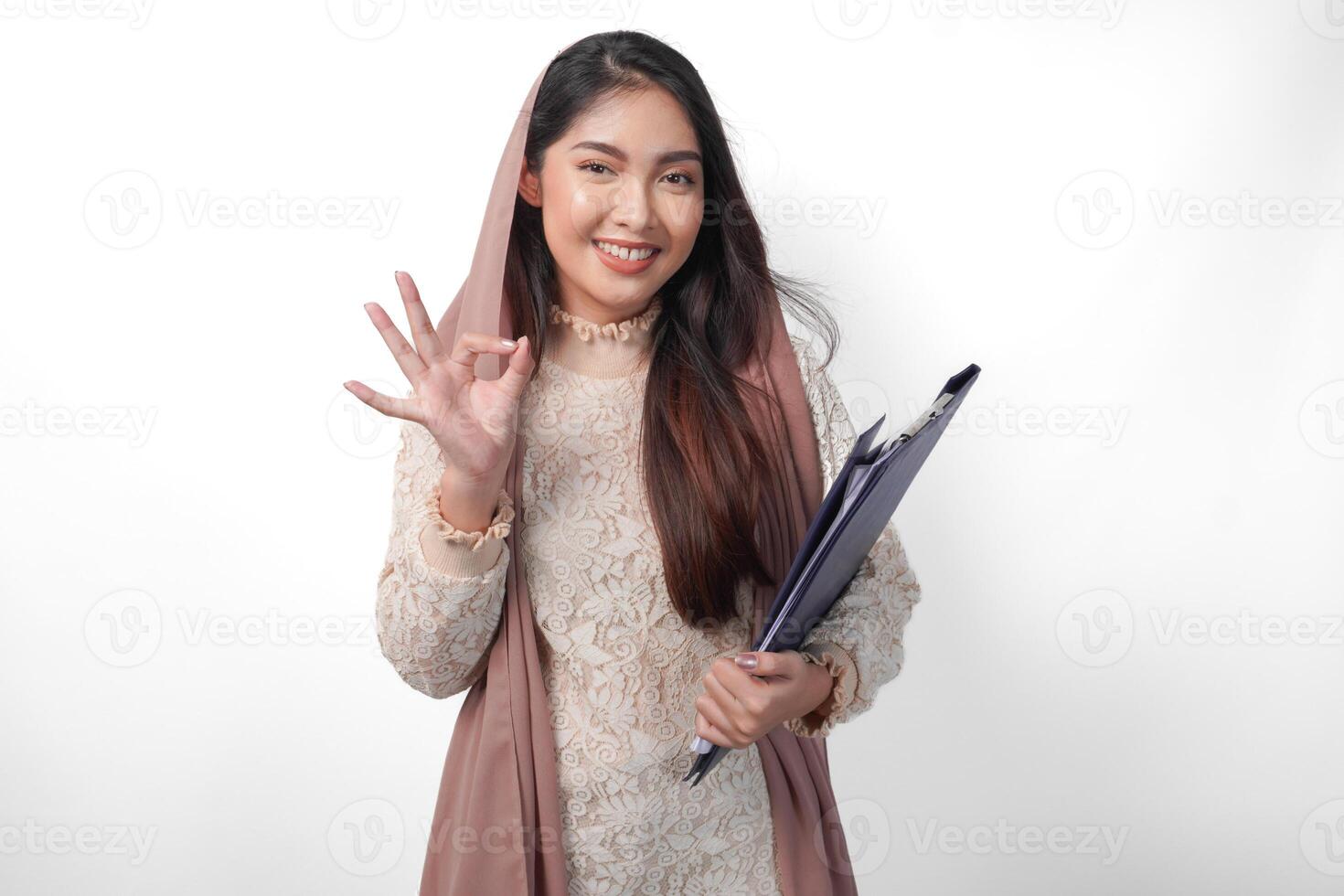 sonriente asiático musulmán mujer en Pañuelo velo hijab participación documentos mapa mientras haciendo un bueno firmar gesto. Ramadán concepto foto