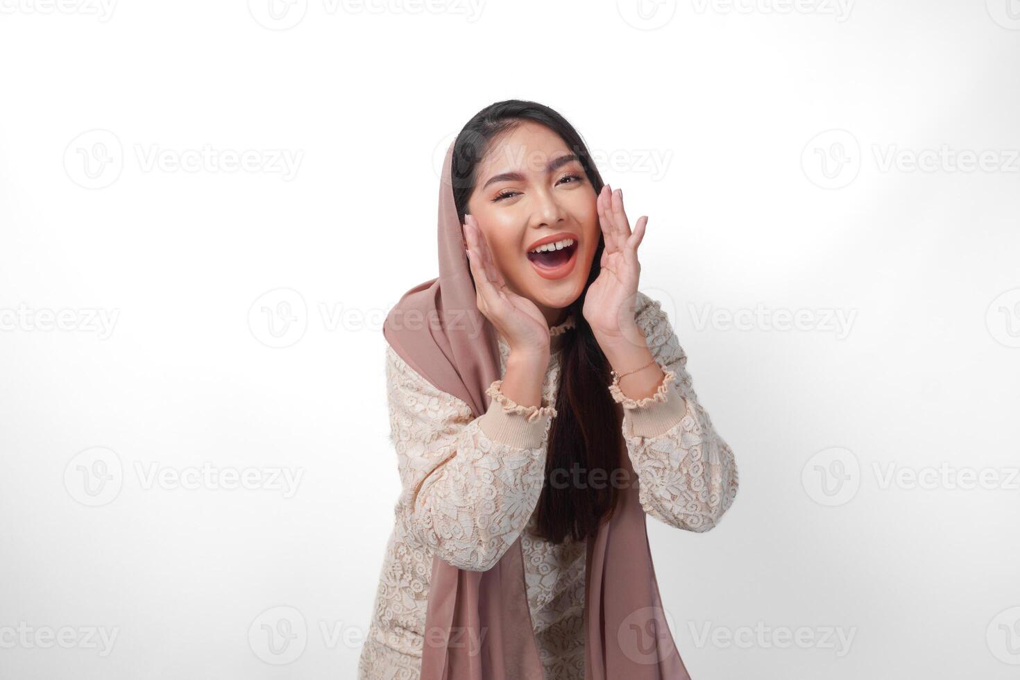 Young Asian Woman wearing headscarf veil hijab is raising hands and shouting with mouth wide open, isolated white background photo