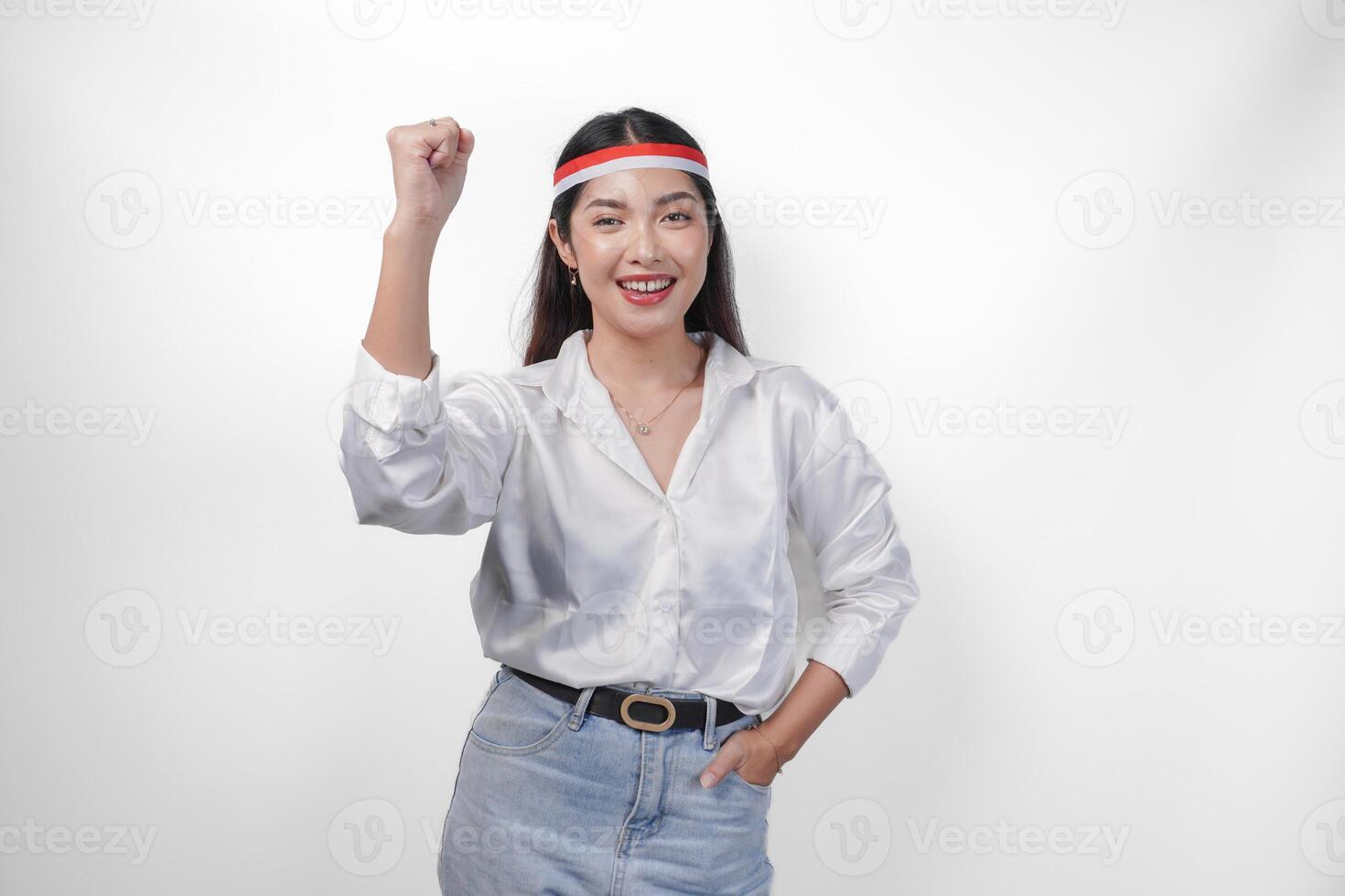 emocionado joven asiático mujer vistiendo país bandera venda y apretando manos mientras celebrando indonesio independencia día aislado en blanco antecedentes foto