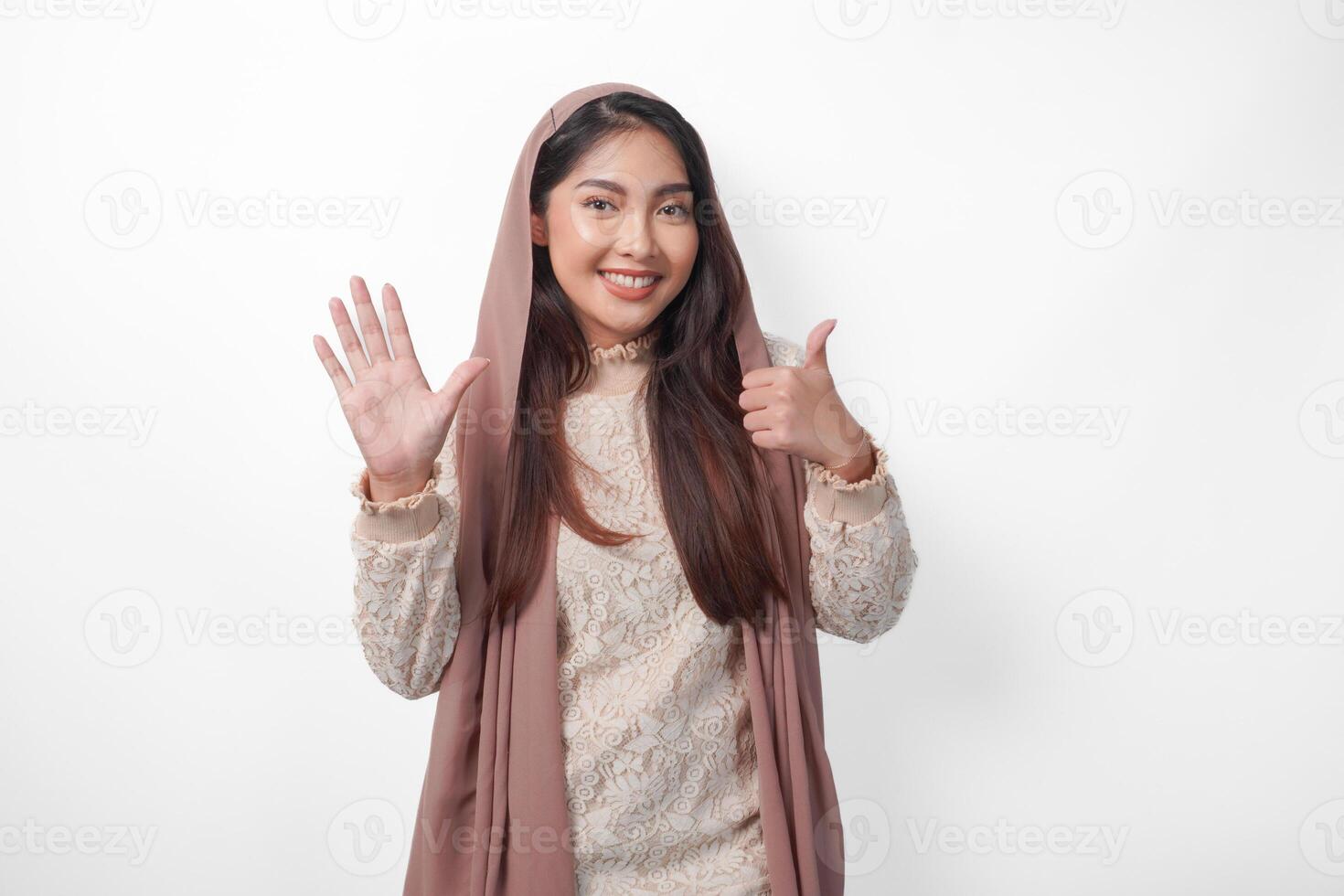 Portrait of attractive Asian Muslim woman wearing veil hijab giving number one to ten by hand gesture, standing over isolated white background photo