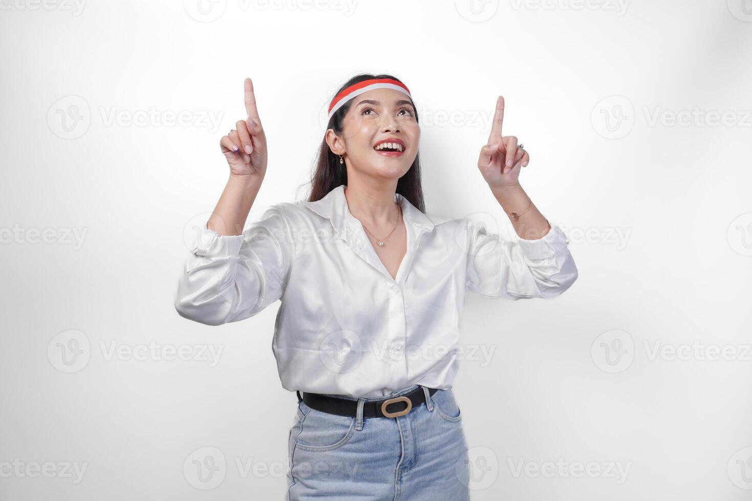 contento asiático mujer vistiendo Indonesia bandera de colores venda y casual atuendo mientras sonriente alegremente y señalando arriba el Copiar espacio hacia arriba. independencia día anuncio concepto foto