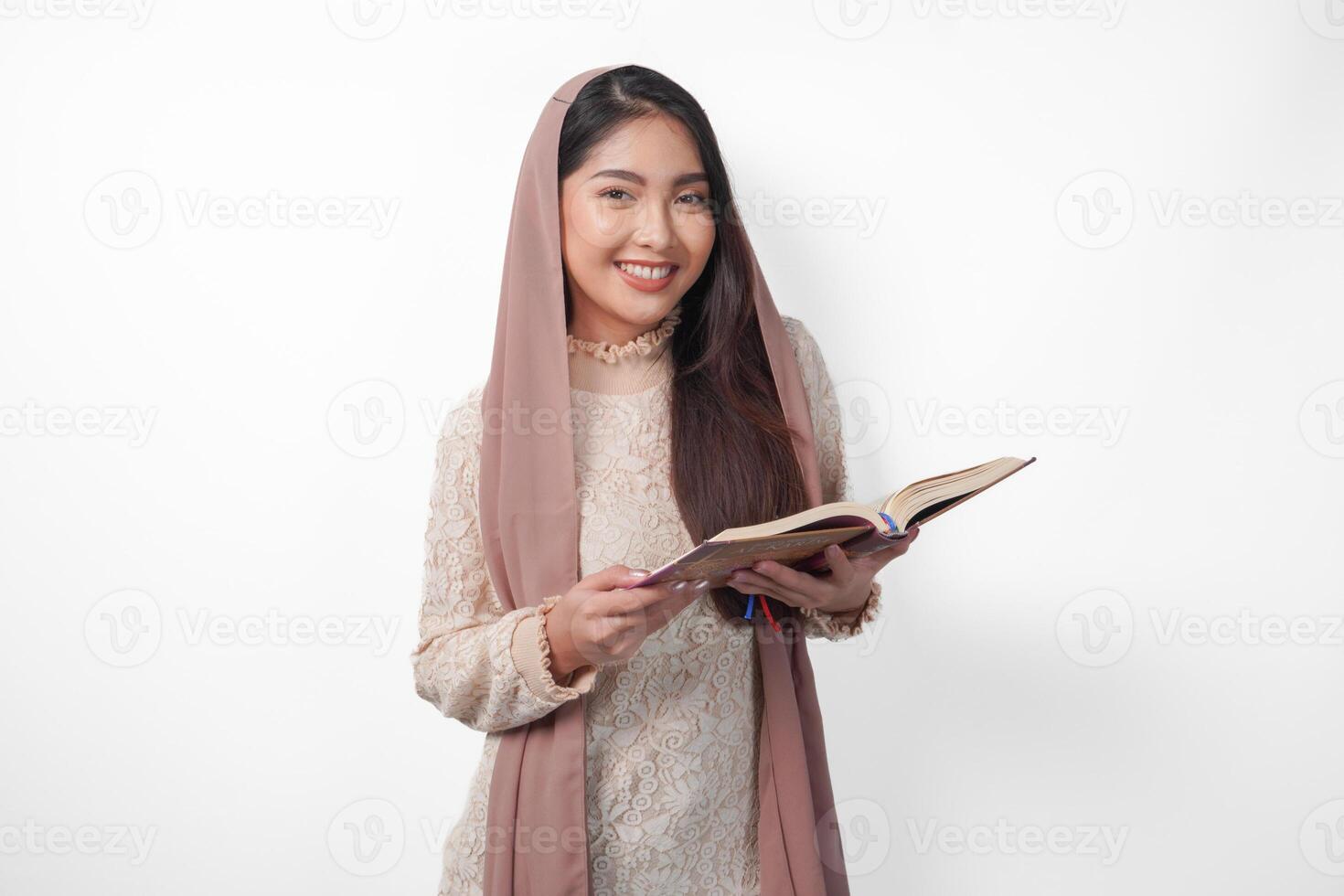 Portrait of a young Asian Muslim woman in veil hijab smiling to the camera while holding Al Quran. Ramadan and Eid Mubarak concept photo
