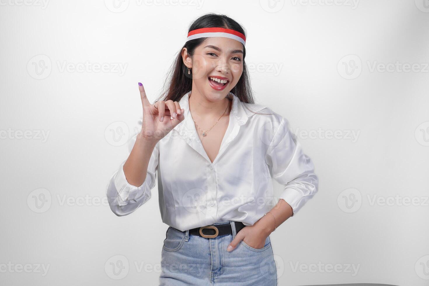 joven asiático mujer con orgullo demostración pequeño dedo sumergido en púrpura tinta después votación para presidente y parlamento elección, expresando emoción y felicidad, vistiendo bandera venda y blanco camisa foto