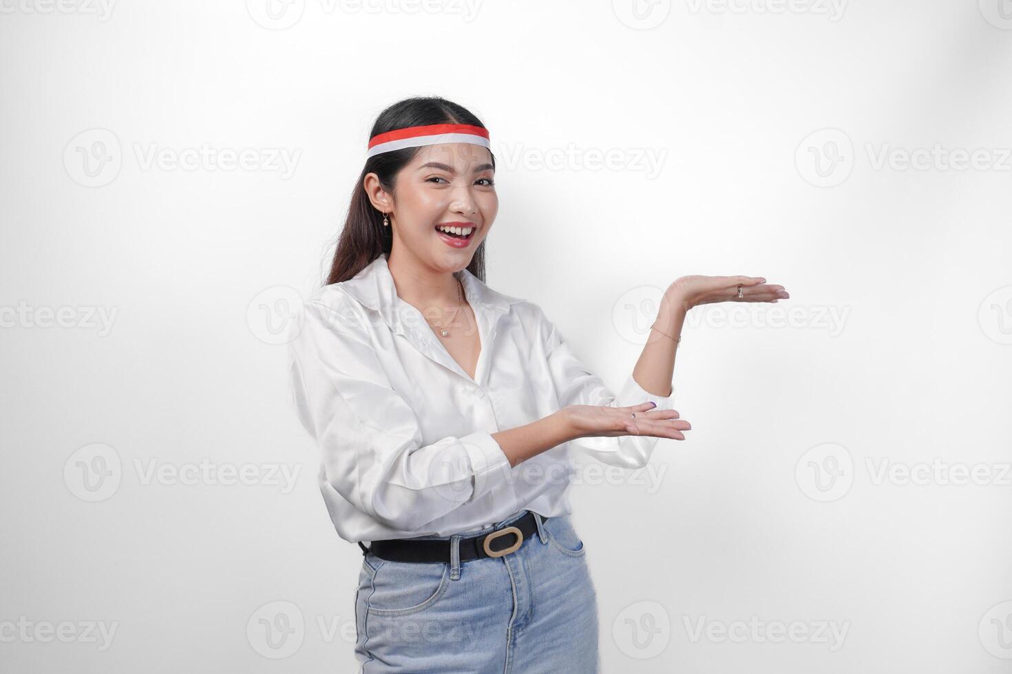 Excited Asian woman wearing flag headband presenting and pointing at the copy space on the side, smiling wide and standing on isolated white background. Independence day advertisement concept photo