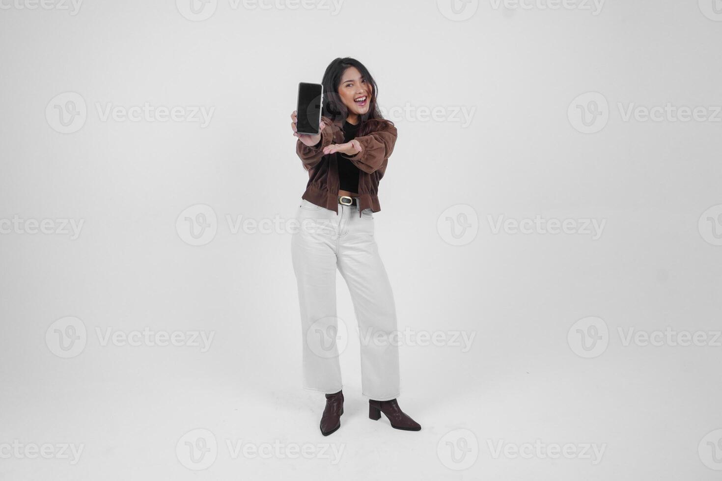 Young Asian woman smiling wide looking happy and holding smartphone while wearing casual outfit standing on isolated white background photo