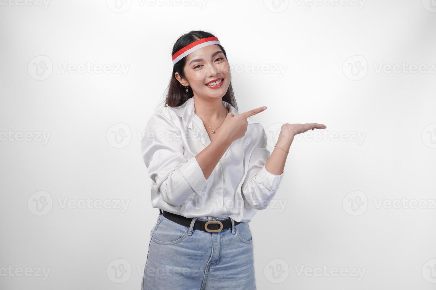 Excited Asian woman wearing flag headband presenting and pointing at the copy space on the side, smiling wide and standing on isolated white background. Independence day advertisement concept photo