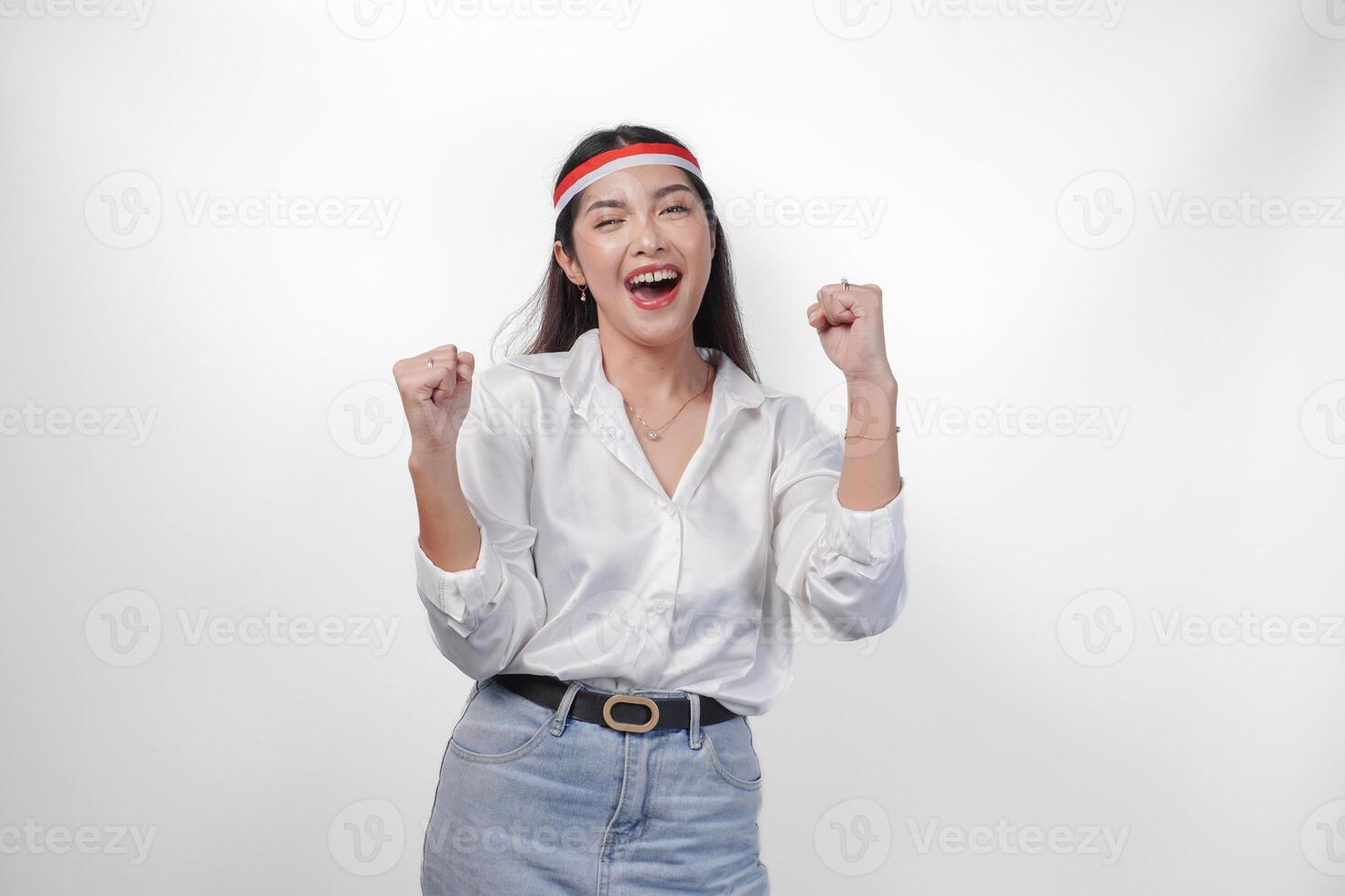 retrato de un emocionado joven asiático mujer levantamiento puño arriba gesto, victorioso y celebrando victoria pose, vistiendo bandera venda y blanco camisa. independencia día concepto foto