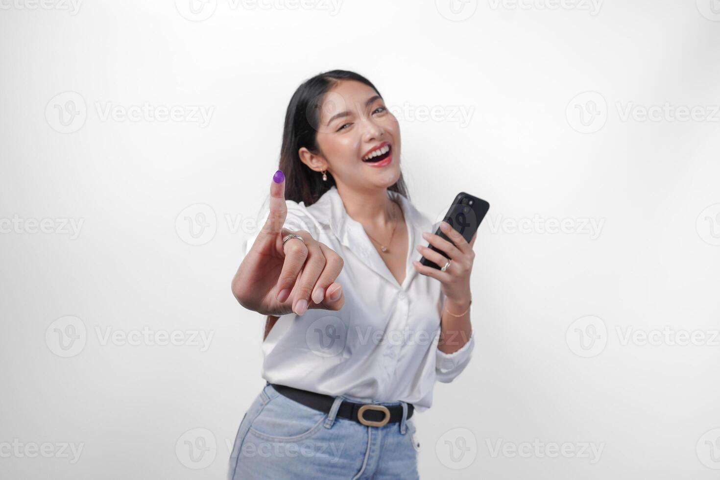 Cheerful Asian woman proudly showing little finger dipped in purple ink after voting for president and parliament election while left hand holding phone, expressing excitement and happiness photo