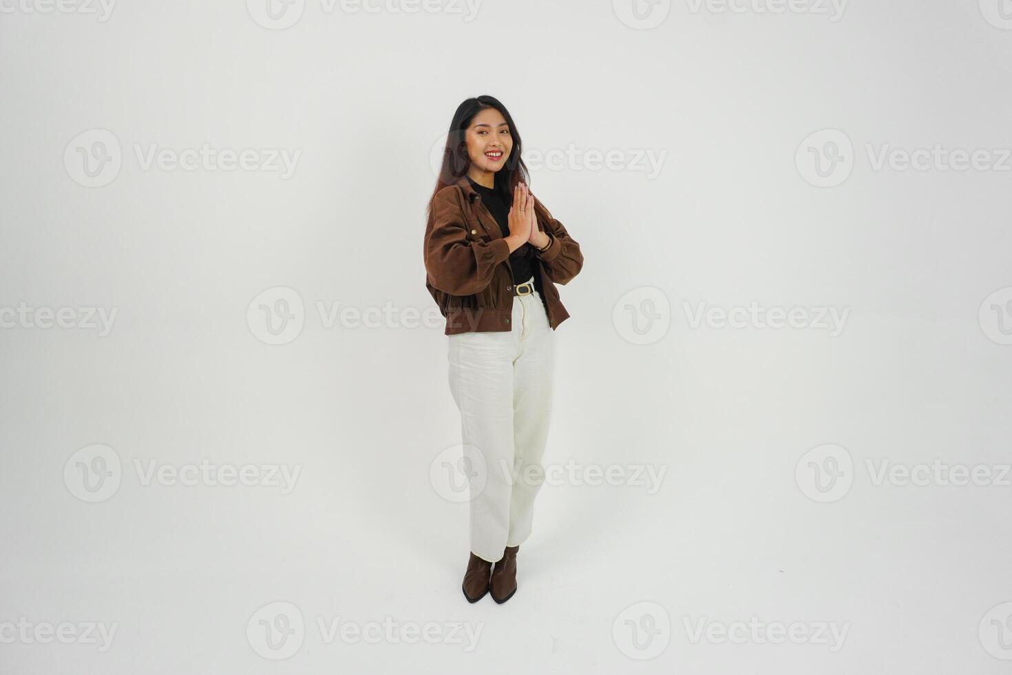 A full body portrait of Asian young woman with casual outfit making greeting gesture with two hands while smiling, standing on isolated white background photo