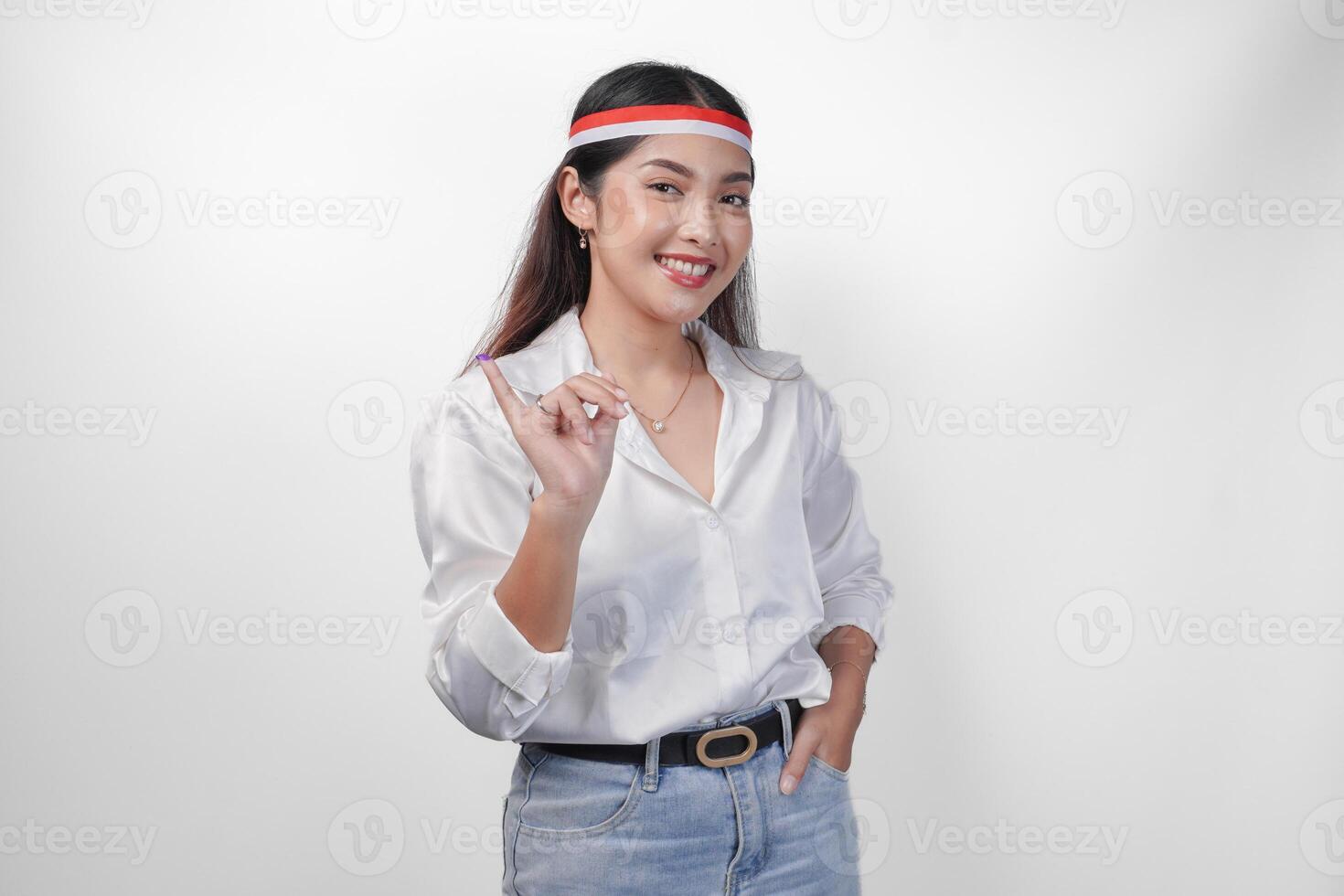 Young Asian woman proudly showing little finger dipped in purple ink after voting for president and parliament election, expressing excitement and happiness, wearing flag headband and white shirt photo