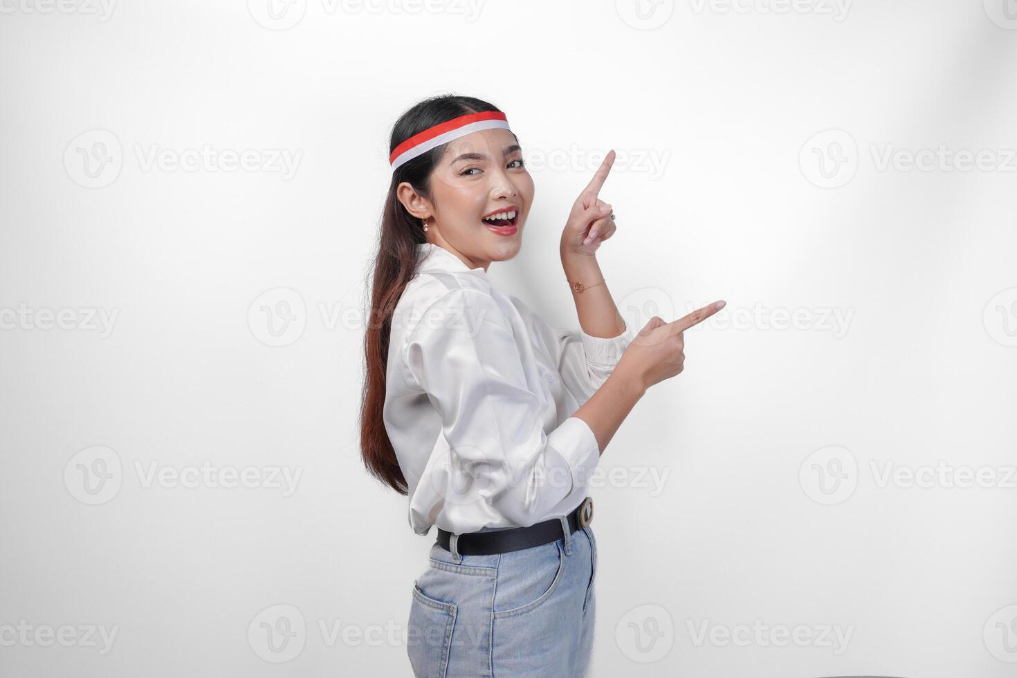 Excited Asian woman wearing flag headband presenting and pointing at the copy space on the side, smiling wide and standing on isolated white background. Independence day advertisement concept photo