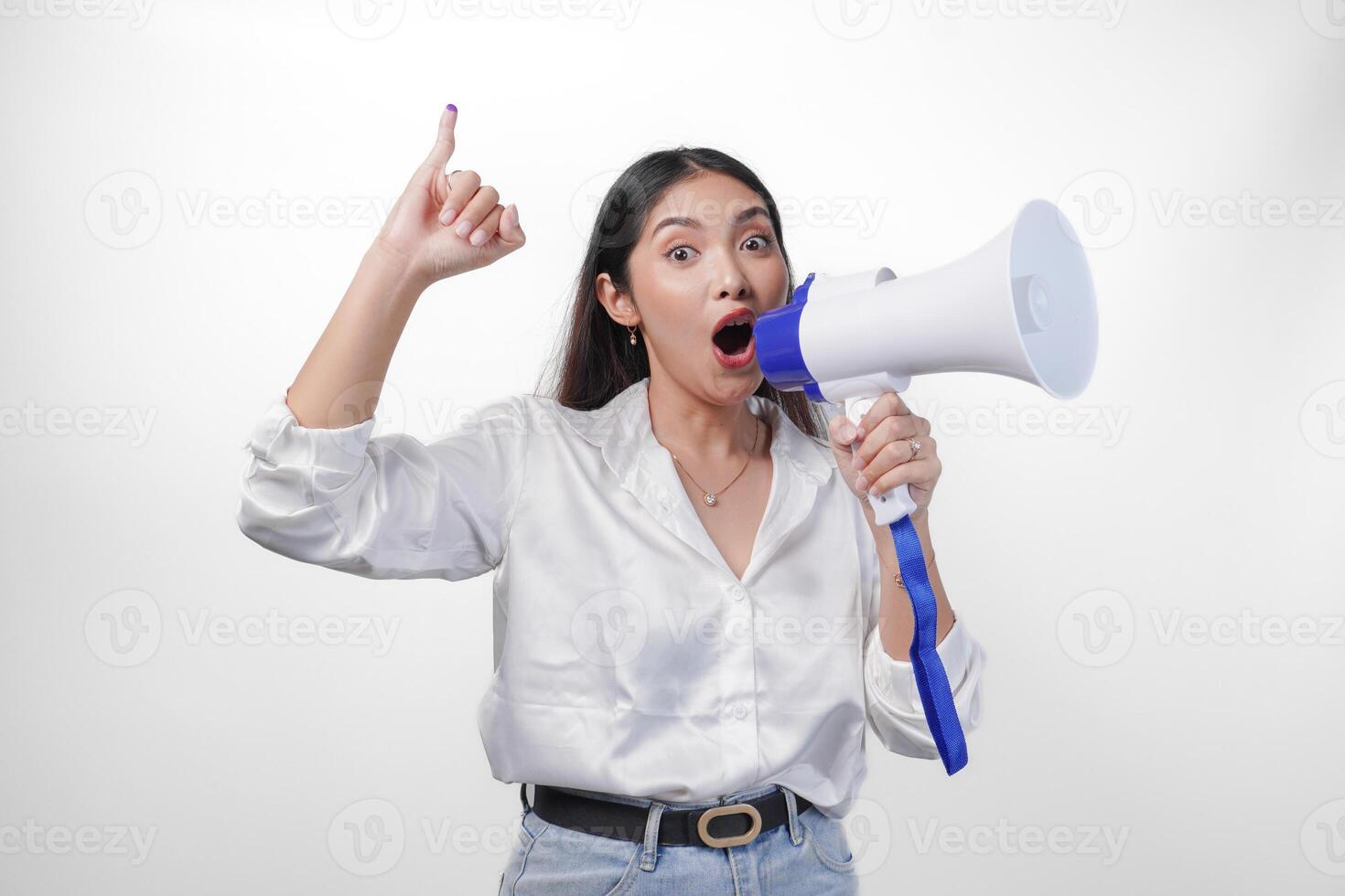 Excited Asian woman in casual formal outfit holding and shouting at megaphone, pointing little finger dipped in purple ink after voting for Indonesia election, standing on isolated white background photo