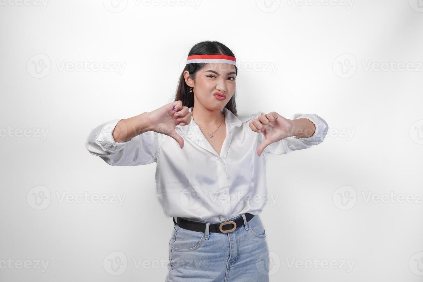 Unhappy Asian woman giving thumbs down gesture with negative expression and disapproval, wearing flag headband and white shirt standing over isolated white background photo