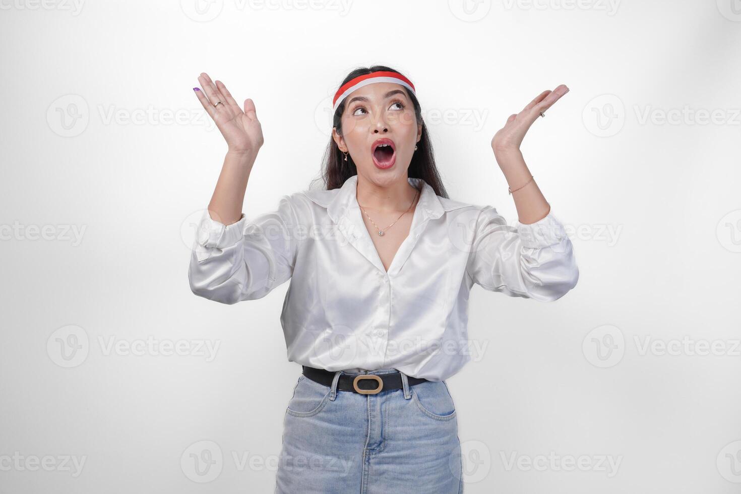 Surprised Asian woman wearing Indonesia flag colored headband and casual outfit while pointing up the copy space upwards. Independence day advertisement concept photo