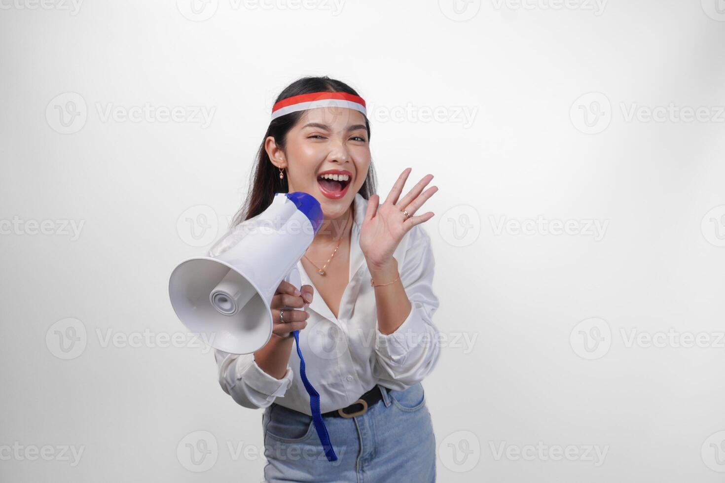 Energetic Asian woman in casual formal outfit wearing country flag headband while holding and shouting at megaphone, standing on isolated white background photo