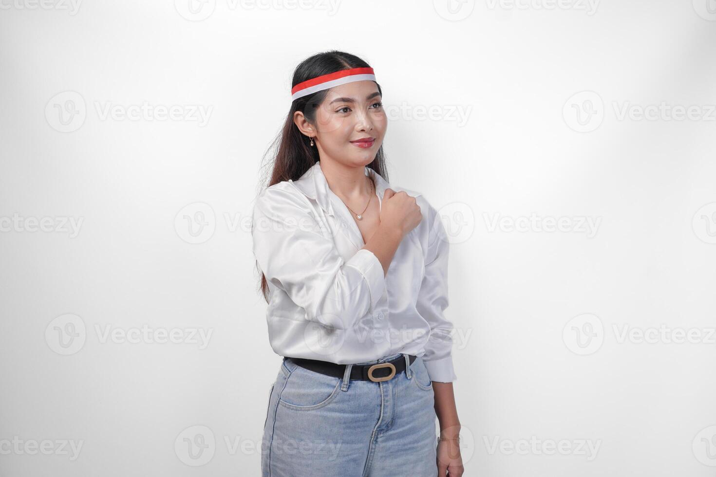 Beautiful Asian woman wearing flag headband with fist on chest celebrating Indonesia Independence Day, standing over isolated white background. Independence day advertisement concept photo
