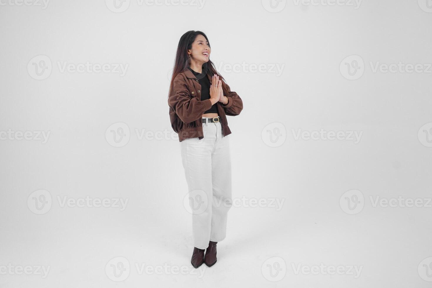 un lleno cuerpo retrato de asiático joven mujer con casual atuendo haciendo saludo gesto con dos manos mientras sonriente, en pie en aislado blanco antecedentes foto