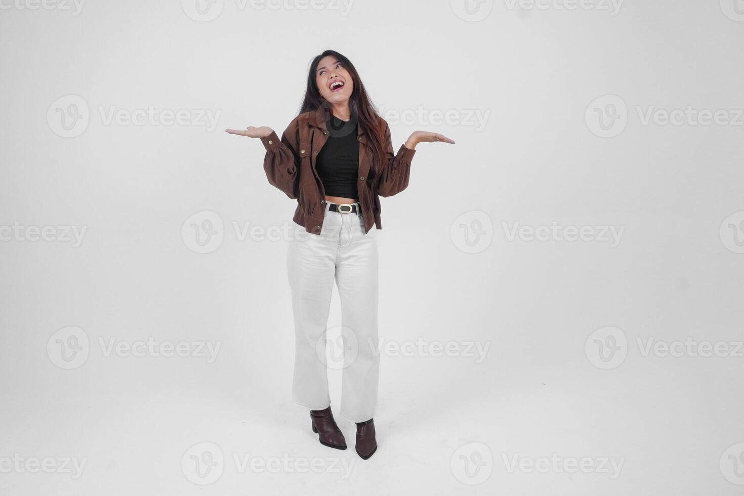 Smiling young Asian girl wearing brown jacket is standing and pointing to a copy space beside her. photo