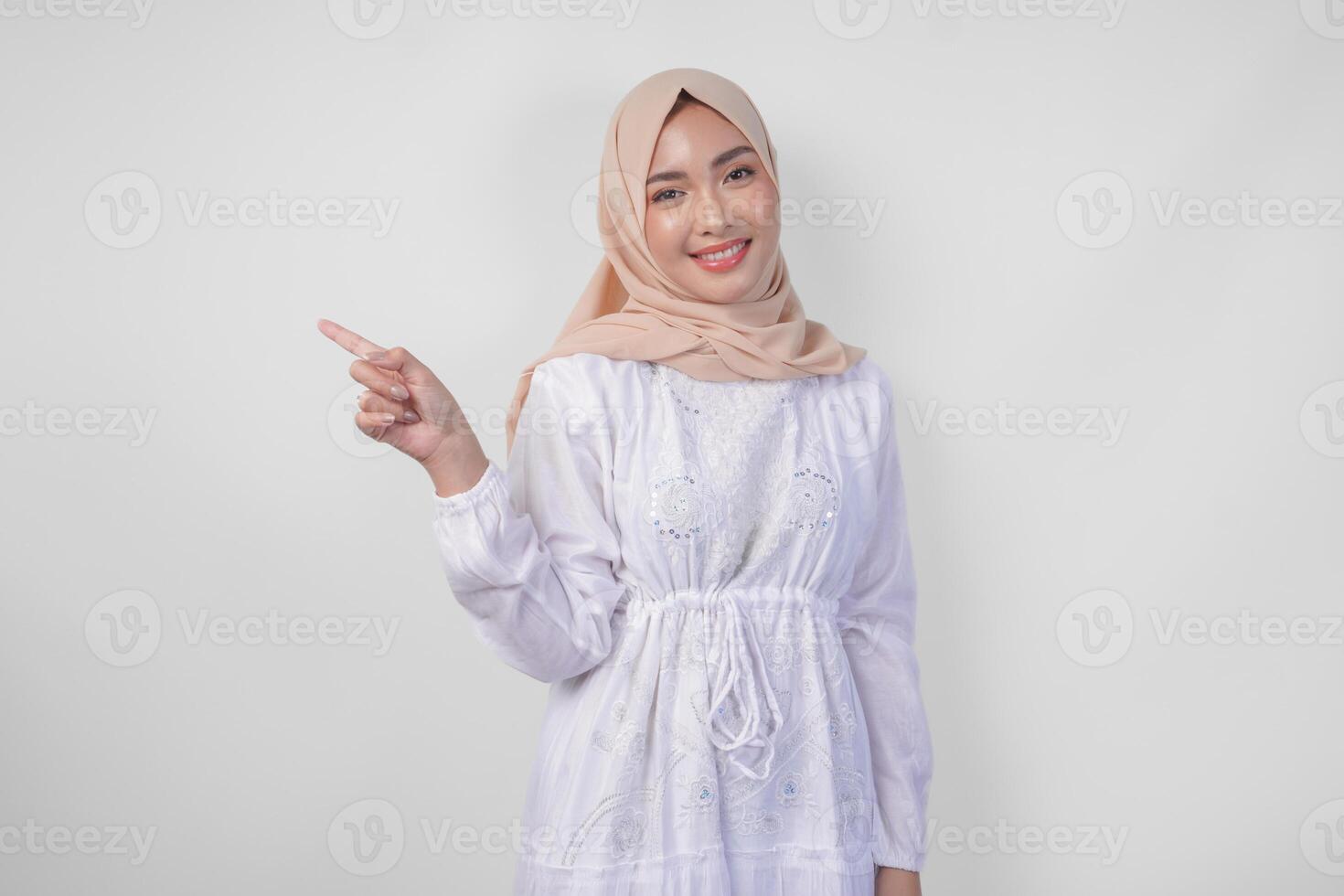 sonriente asiático mujer vistiendo hijab y blanco vestir señalando arriba a el Copiar espacio en su Derecha lado, en pie terminado aislado blanco antecedentes. Ramadán y eid Mubarak anuncio concepto foto