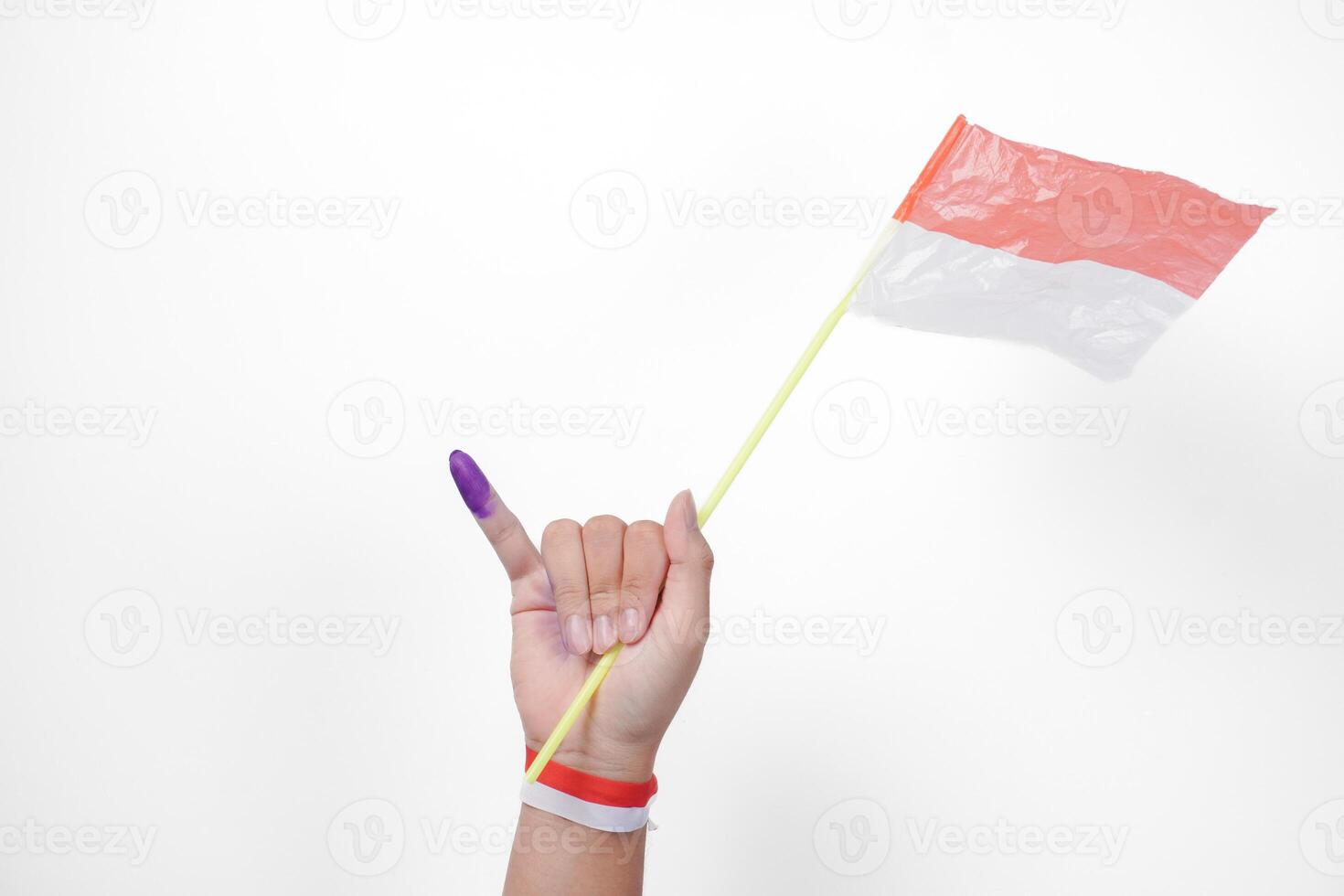 Group of hand wearing flag ribbon on wrist showing little finger dipped in purple ink after voting for Indonesia Election or Pemilu while holding mini flag, isolated over white background photo