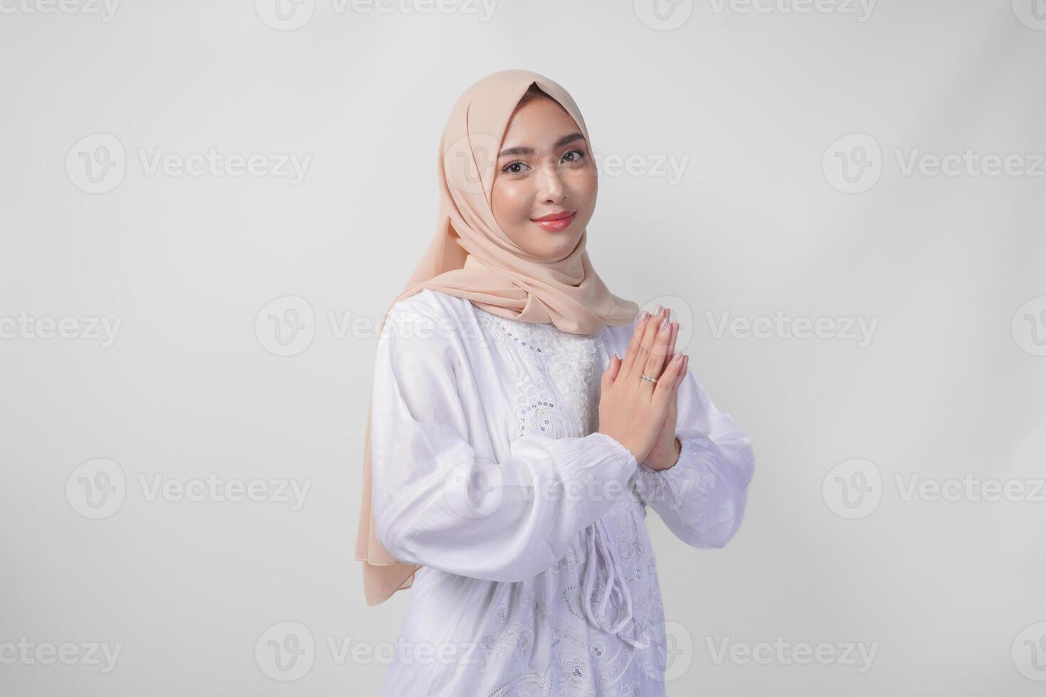 hermosa asiático musulmán mujer vistiendo blanco vestir y hijab sonriente mientras haciendo formal Bienvenido o saludo gesto, en pie terminado aislado blanco antecedentes foto