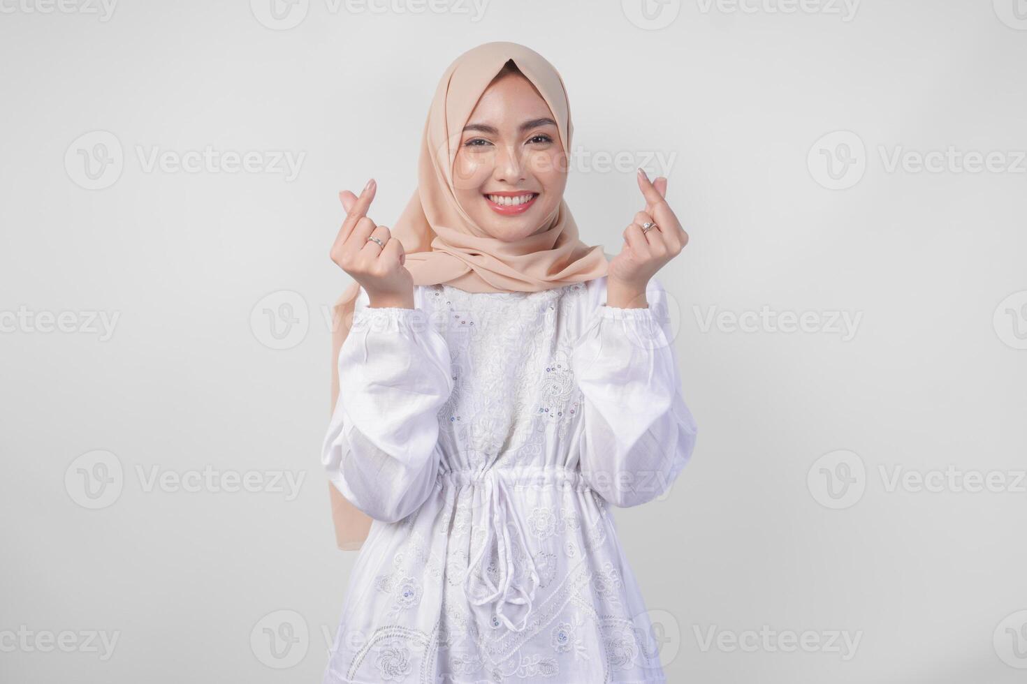 Young Asian Muslim woman in white dress and hijab making a heart love shape gesture with hands in various pose, isolated on white background photo