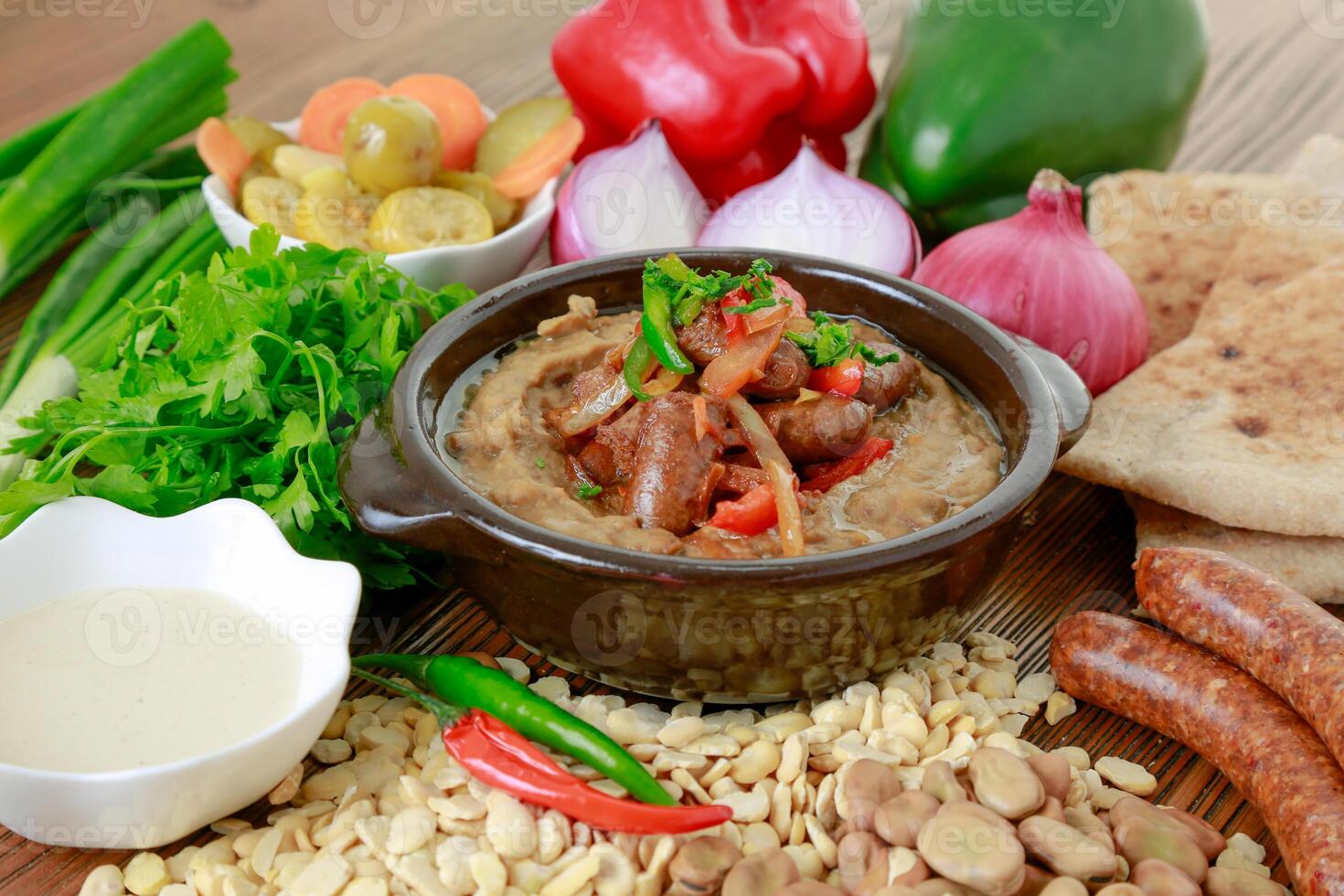 Foul with sausage or mashed beans with bell pepper, onion, tomato, pickle and pita bread served in dish isolated on wooden table side view of arabic food photo
