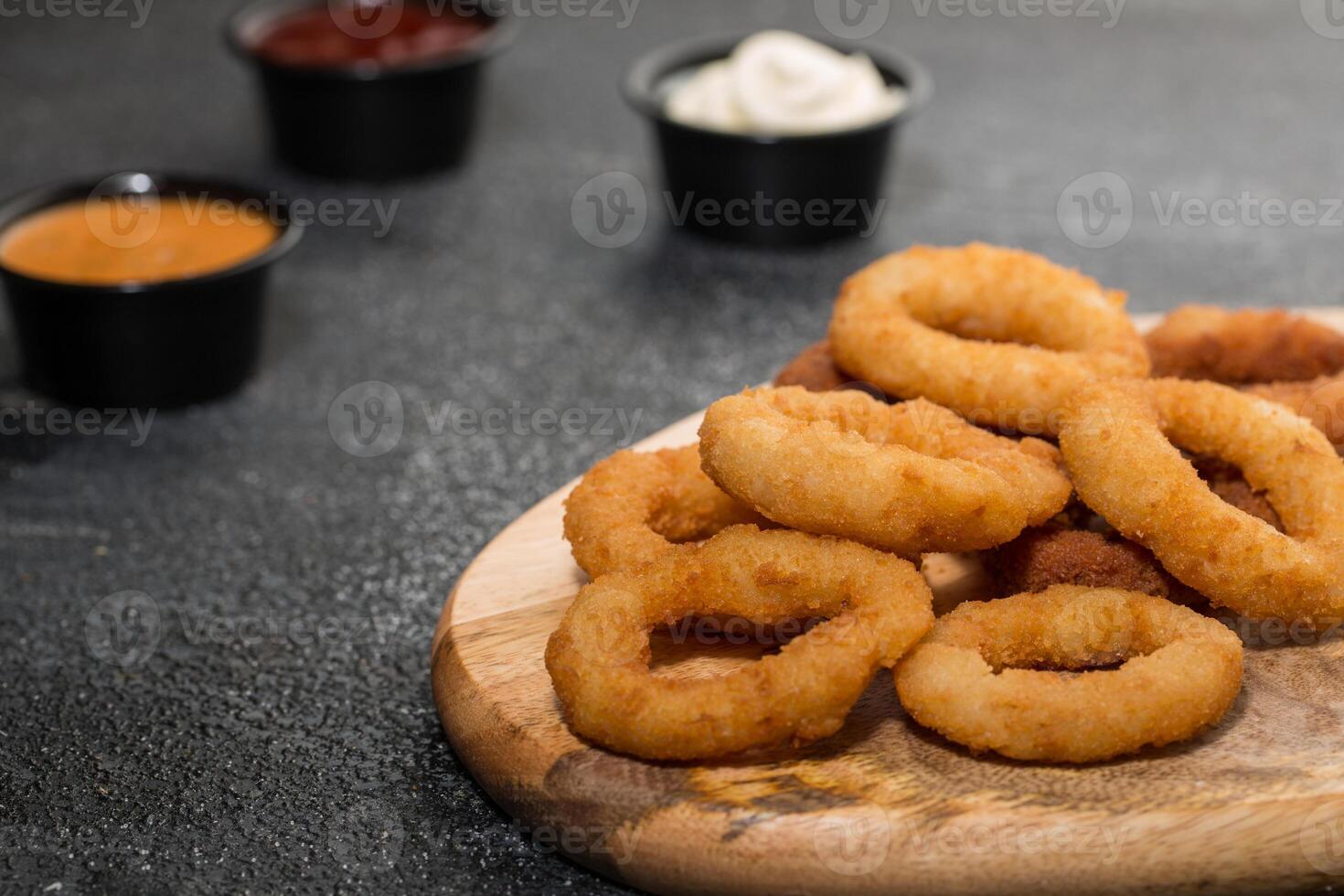 Crunchy Onion Rings with dip sauce and mayonnaise isolated on wooden board with dip sauce top view of grill food on dark grey background photo