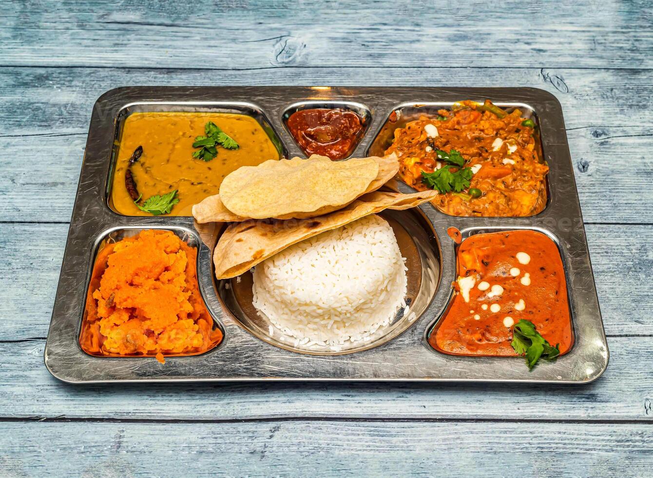 north indian vegetarian meal thali with curry, rice, chapati and vegetables served in dish isolated on wooden table top view of indian spicy food photo