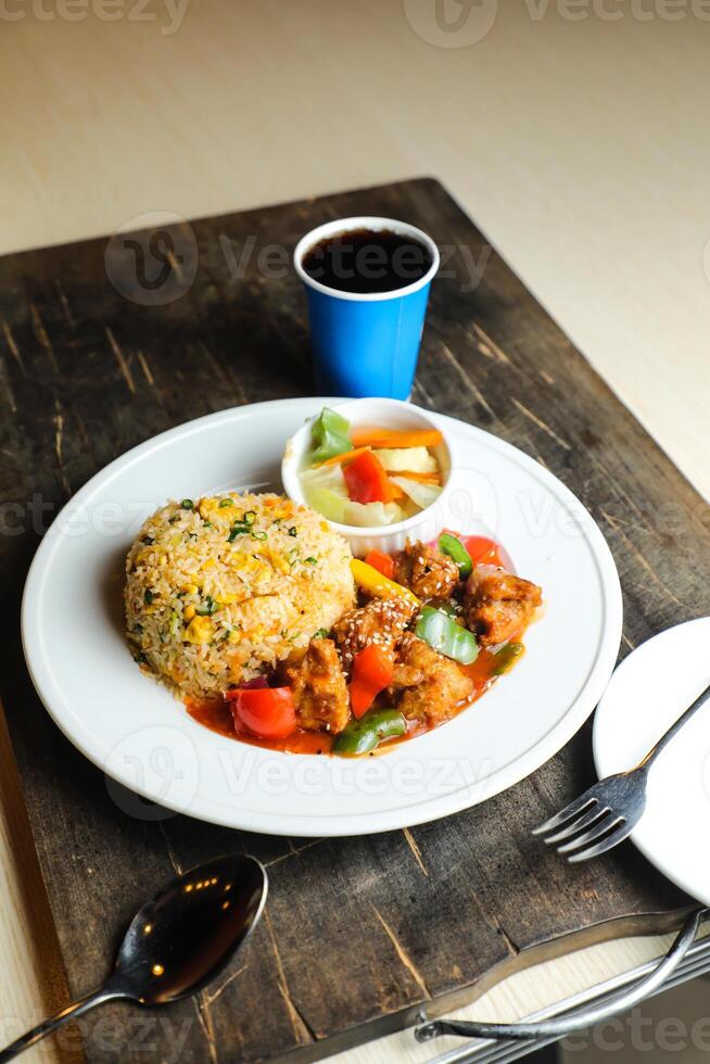 Chili Chicken Rice Meal served in plate with sauce, cold drink, spoon and fork isolated on wooden board side view of thai food photo