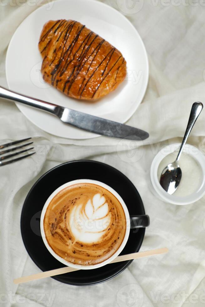 Hot Macchiato Coffee Latte Art served in cup with croissant, puff pastry, bread and knife isolated on napkin top view cafe breakfast photo