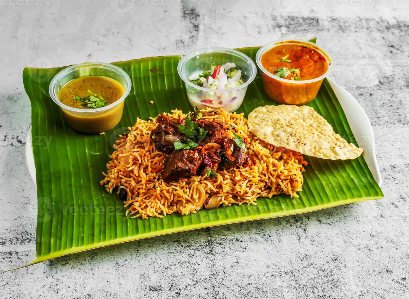 mutton briyani rice pulao with salad, chutney, raita and sauce served in dish isolated on banana leaf top view of indian and singapore spicy food photo