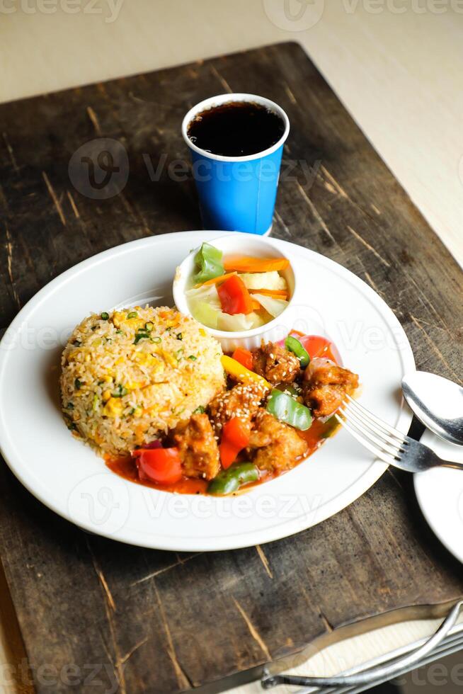 Chili Chicken Rice Meal served in plate with sauce, cold drink, spoon and fork isolated on wooden board side view of thai food photo