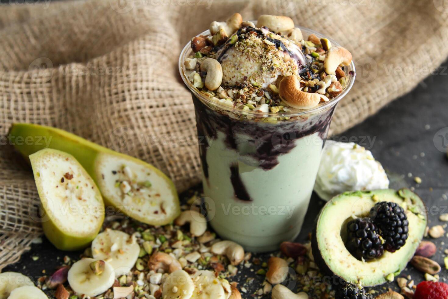 Ice cream shake with nuts, banana, mulberry, raspberry, avocado, pistachio and cashew nut served in disposable glass isolated on table side view of healthy drink photo