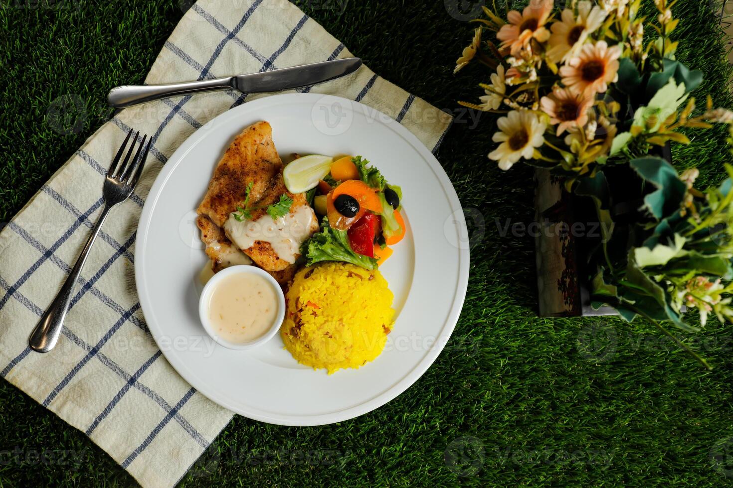 Grilled Jerk Spiced Fillet Fish with rice, dip and salad served in plate with knife and fork isolated on napkin top view of korean style meat food on gassy background photo