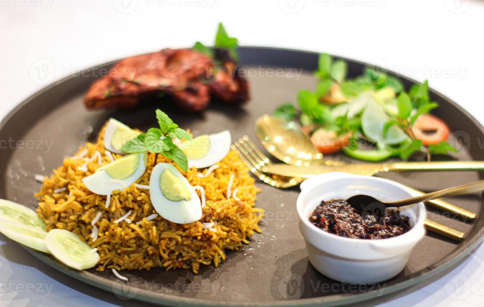 Grilled Chicken tikka biryani rice with egg, salad, spoon, fork and knife served in dish isolated on table side view of indian spices food photo